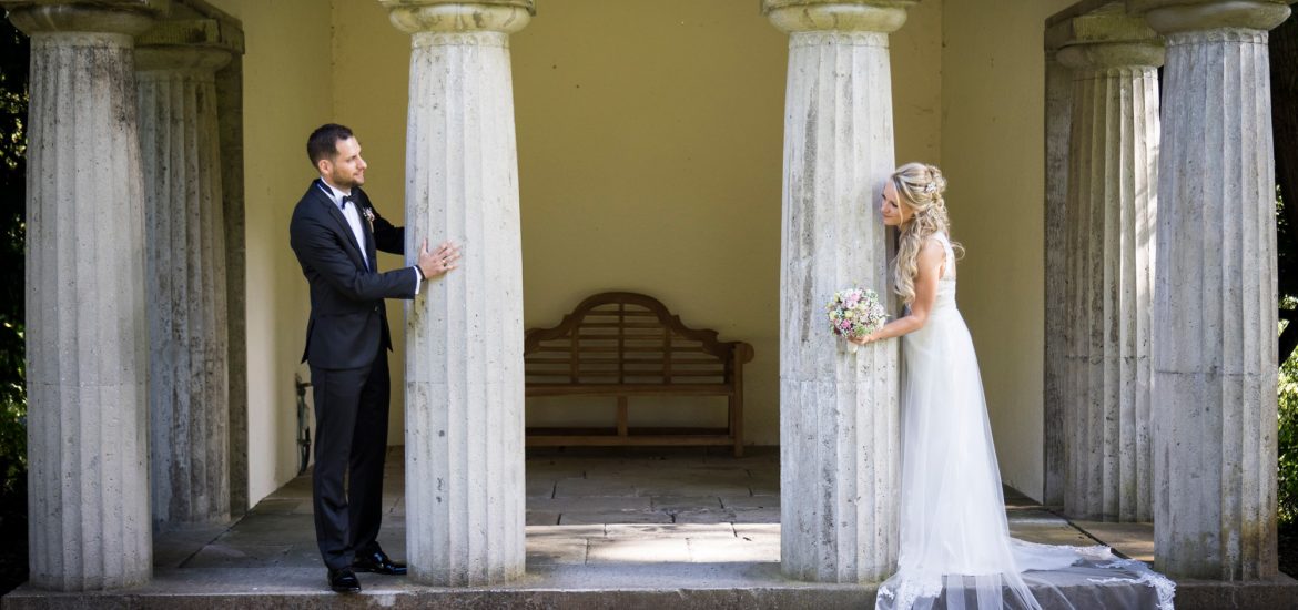 Das Brautpaar steht hinter zwei nebeneinander stehenden Säulen und schaut sich an