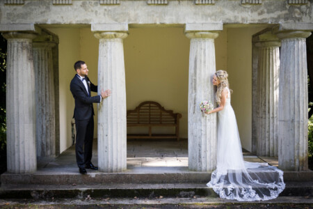 Das Brautpaar steht hinter zwei nebeneinander stehenden Säulen und schaut sich an Griechische Säulen