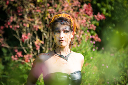 Rot, Schwarz geschminkte Frau vor Strauch mit roten Blüten Feuer vor dem brennenden Busch